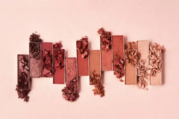 Flat lay of broken shimmering brown and nude eye shadow palette on a beige background. Cosmetic beauty product