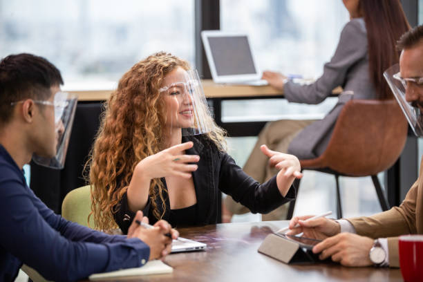 istock Businesswoman in face shield explaining work project to colleagues in the office. group of business financial discussing project. Corporate team brainstorming and sharing idea. 1372162115