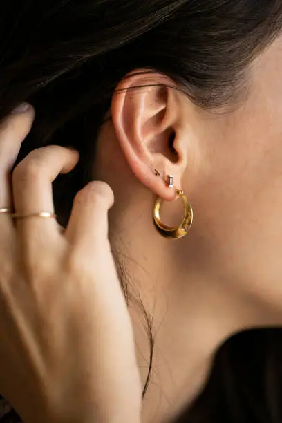 Close up of young woman holding black hair while wearing gold hoop earring and small diamond stud