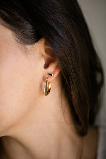Close up of woman wearing one gold hoop earring and one small diamond stud earring.