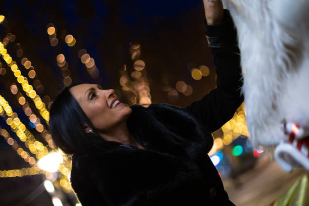 Girl posing at Christmas lights decoration on night street closeup. Happy woman enjoying illuminated fair at xmas celebration outdoors. Cheerful lady looking camera standing festive fairground alone.