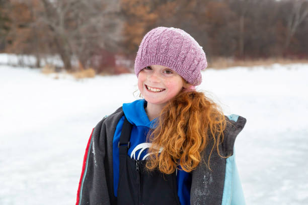 Close-up of a young girl on frozen lake ice in the snow on a winter day. She is looking at the camera and smiling.