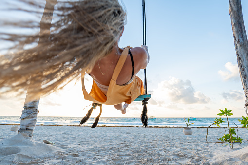 View of woman swinging on white sand beach relaxing in Mexico