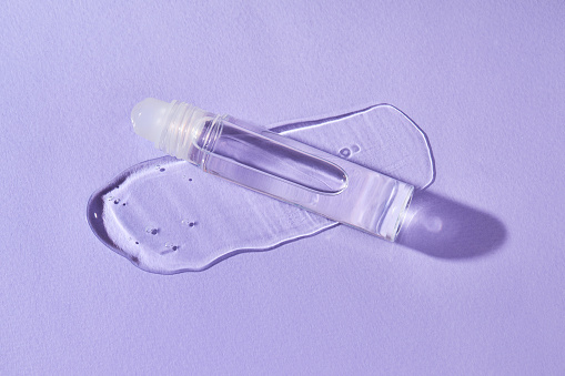 Brillo de labios transparente en una bola de rodillo botella sobre un fondo púrpura. photo