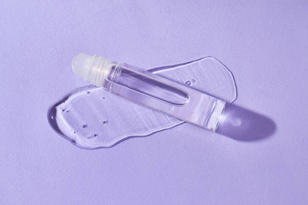 Transparent lip gloss in a roller ball bottles on a purple background.