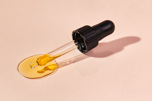 Close up of pipette with pouring liquid essential oil on beige background. Dropper with a falling drop of aromatherapy oil close-up