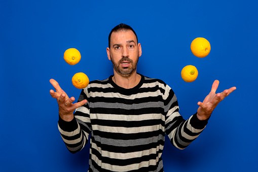 Funny man in striped sweater, posing isolated on blue wall background, studio portrait. Healthy fashion lifestyle, people emotions, cold season concept. Mock up copy space. throwing lemons