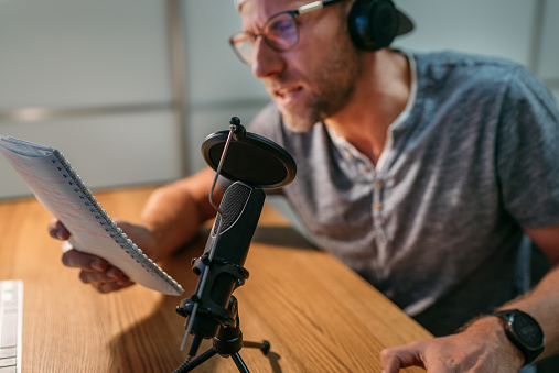 Microphone with pop filter closeup photo with blogger man in headphones recording voice or making online webinar or news announcement. Modern home sound studio audio recording technology concept.