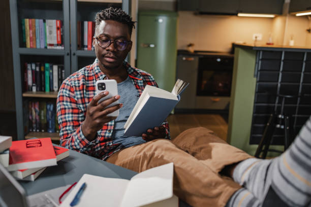 istock African-American man reading a book and using mobile phone at home 1372181844