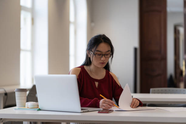 istock Focused asian female student preparing for exam or doing homework in university reading room 1372182246