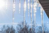 Long shiny icicles hang from the roof in the sunlight. Icicles against a blue sky