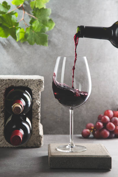赤ワインのボトルは、コンクリートの背景にワイングラスに注がれました。縦書き形式。飲料とワインのコン�セプト。 - wine glass ストックフォトと画像