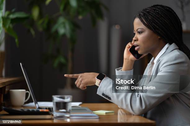 Shocked Unhappy Afro Businesswoman Talk On Phone Call Point Finger At Laptop Screen Solving Problem Stock Photo - Download Image Now