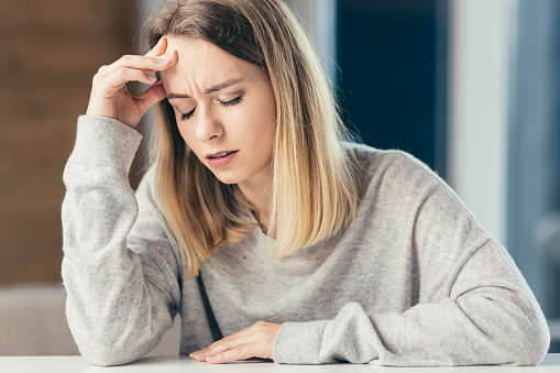 The young woman has a headache, holds her head with her hands and shows pain at home, in the office at work