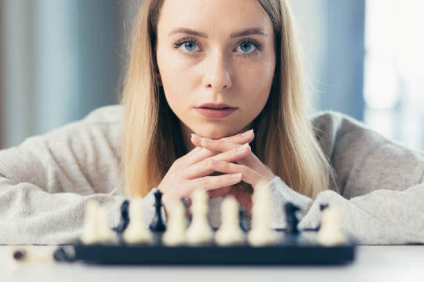 retrato fotográfico en primer plano de una joven hermosa mujer jugando al ajedrez en casa, estudiando, pensando, compitiendo, en cuarentena - concentration chess playing playful fotografías e imágenes de stock