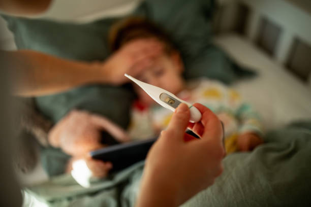 Mother taking care of sick child Close up of mother taking care of her sick child in cozy bright and warm kids bedroom with pastel green background in sunny morning light. Little girl has a cold and her mother is measuring her temperature with digital thermometer . fever stock pictures, royalty-free photos & images