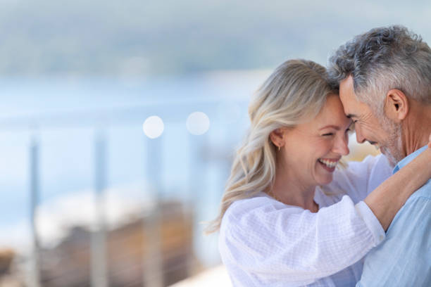 Mature couple dancing at a waterfront home or holiday villa. Mature couple dancing at a waterfront home or holiday villa. They are smiling and having fun. Probably on a romantic vacation. The woman has her arms around the man. The ocean is in the background middle aged couple dancing stock pictures, royalty-free photos & images