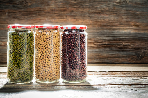 Assorted soybeans soy beans legumes in glass jar in a row on rustic wooden background as: white soybean, mung bean and adzuki bean