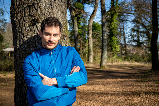 The man is training in the woods and is leaning against an oak tree.