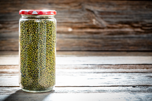 Dried green soybeans, mung beans legumes in a glass jar closeup isolated on rustic wooden background