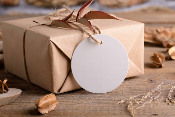 istock Round white gift tag mockup on craft wrapped presents on rustic wooden background with boho decoration 1372193367