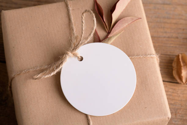 istock Round white gift tag mockup on craft wrapped presents on rustic wooden background with boho decoration 1372193369