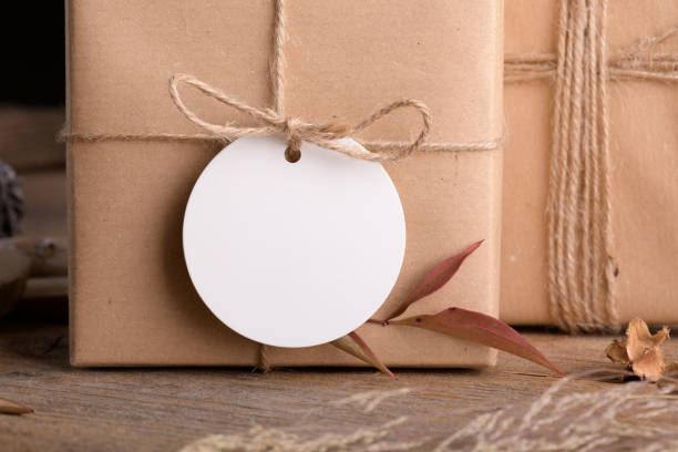 istock Round white gift tag mockup on craft wrapped presents on rustic wooden background with boho decoration 1372193377
