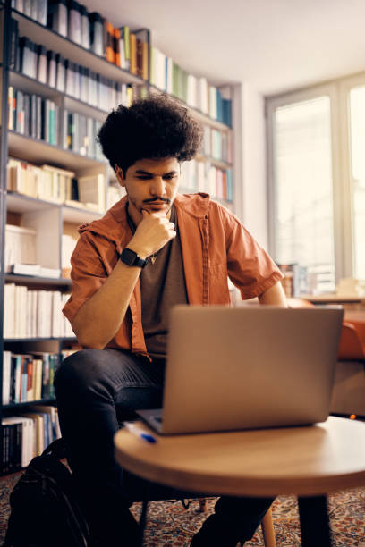 istock Young pensive Muslim man e-learning over laptop at university library, 1372197849