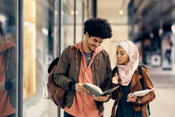 Happy Muslim student and his female friend going through notes after the lecture at campus. Happy Middle Eastern couple reading lecture notes after the class at the university. north african ethnicity stock pictures, royalty-free photos & images