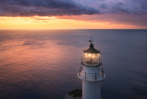 여름에 화려한 일몰에 산 봉우리에 등대. 공중 보기. 밤에 보라색 구름과 아름다운 등대, 빛, 바다와 오렌지 하늘. 그리스 케이프 레프카다의 최고 전경. 풍경화 - lighthouse 뉴스 사진 이미지