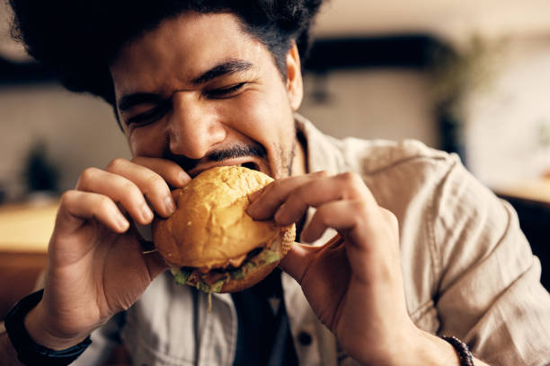 istock Young Muslim man biting cheeseburger while eating in a pub. 1372199790