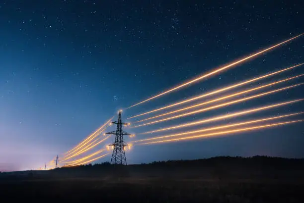 Photo of Electricity transmission towers with orange glowing wires against night sky.
