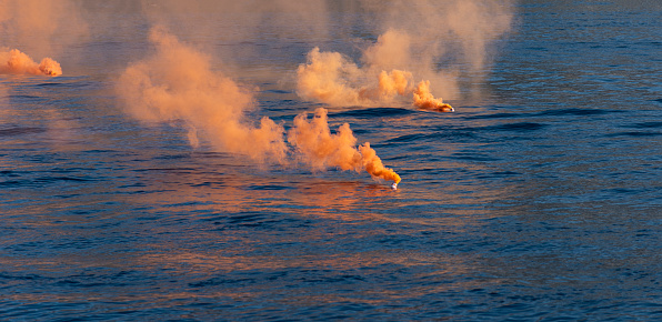 Orange colored smoke grenade in the blue sea. Distress call