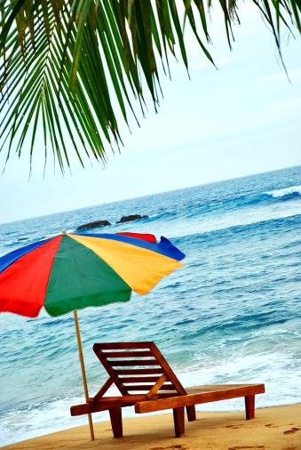 Umbrella and lounge chair on the shore of exotic island with palm trees