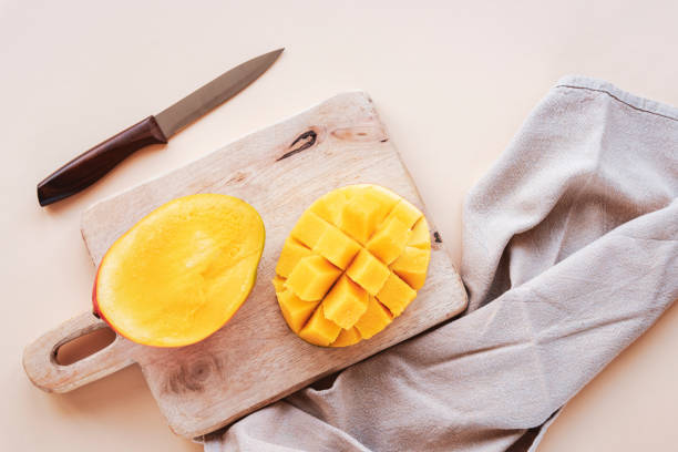 mangohälften auf einem schneidebrett auf beigem backgrownd. draufsicht, flache lage - backgrownd stock-fotos und bilder