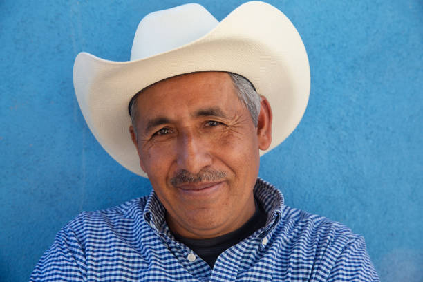 A portrait of a Mexican man wearing a white cowboy hat, against a bold blue background