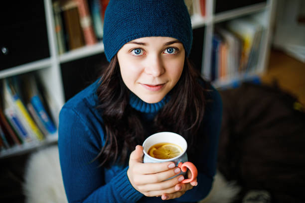 A girl in blue clothes drinks tangerine tea from a blue mug