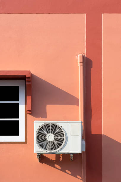 Air conditioner compressor with pipeline installation near white window on brown cement wall of vintage house in vertical frame