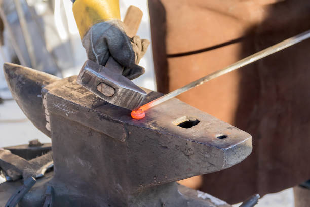 en la mano de un herrero masculino, un martillo de trabajo para trabajar en un yunque con una barra de hierro al rojo vivo. - herramientas de herrero fotografías e imágenes de stock