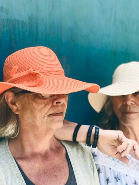 “Thelma and Louise”, but “The senior years”, two sisters bonding in large straw hats outdoors. stock photo