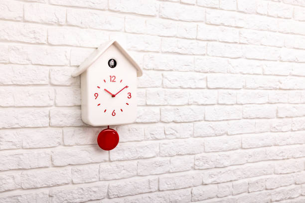 istock Cuckoo bird clock with red pendulum on a white brick wall 1372278523