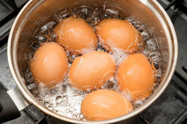 huevos que se hierven en agua hirviendo en una olla - hervir fotografías e imágenes de stock
