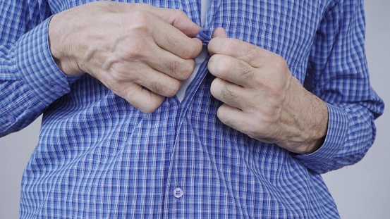 An elderly man struggles to button his clothes.