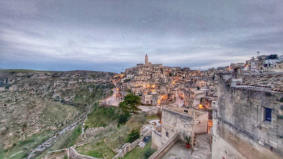 Panorama on the Sassi of Matera at dusk, with small flames lit in front of the doors of the houses.