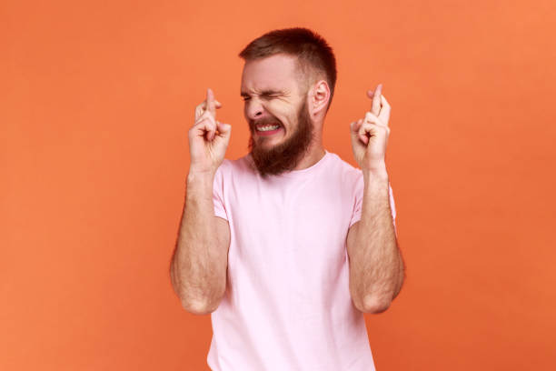 homem cruzando os dedos e fechando os olhos fazendo desejo, acreditando em milagre, esperança no sucesso. - clenching teeth - fotografias e filmes do acervo