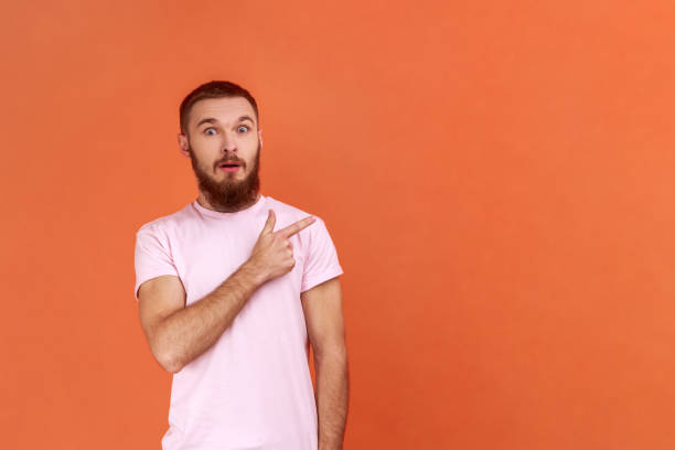 istock Man standing, looking at camera with surprised face and pointing at wall copyspace. 1372288458