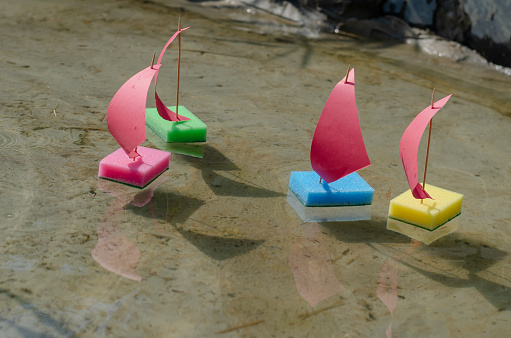 Toy sailboats made from kitchen sponges. Children's sailing regatta in the city fountain. Four children's colorful ships are floating in a shallow pond. Selective focus. No people.