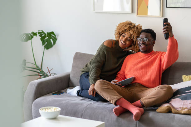 The couple is relaxing on the sofa and watching tv stock photo