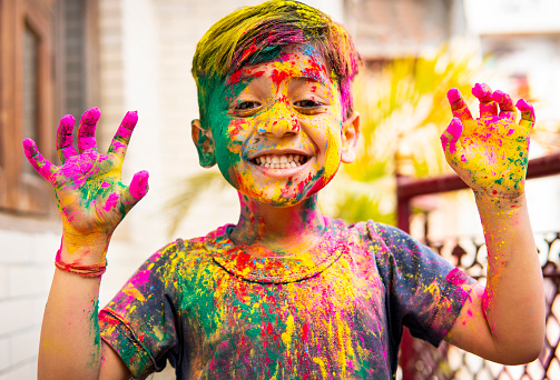 Portrait of cute happy Indian little boy covered with colored powder and celebrating the Holi festival.