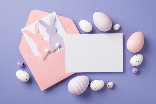 Top view of the pink envelope with two postcards and cute paper rabbits with round tails many eggs different size and color on the pastel violet background